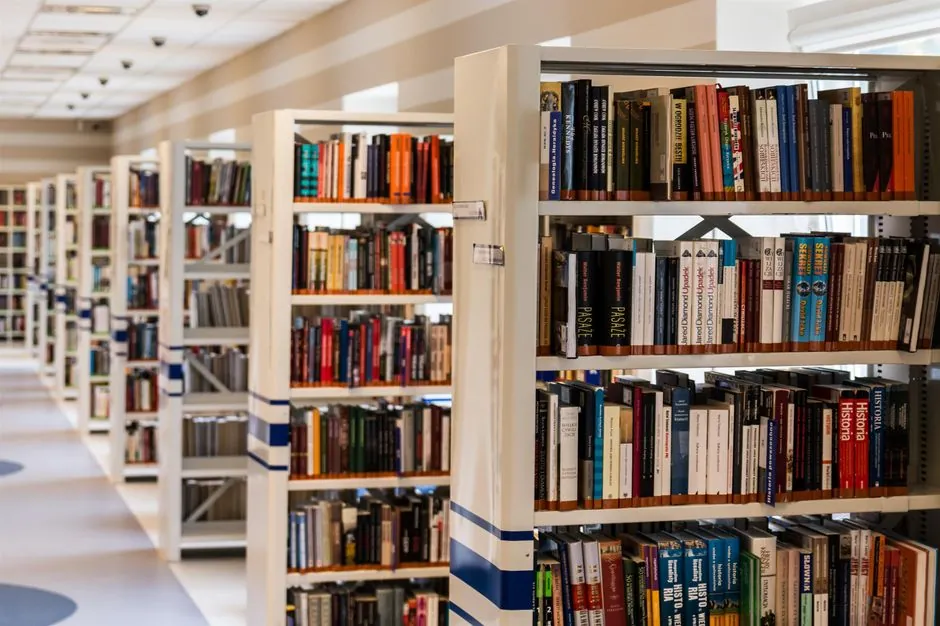 A person reading a dense book in a library with shelves behind